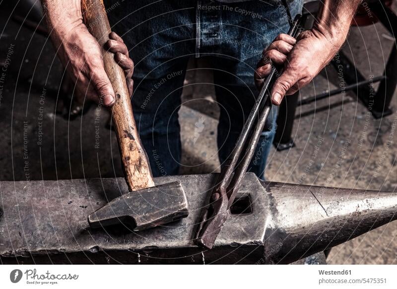 Knife maker holding pliers and hammer on anvil human human being human beings humans person persons caucasian appearance caucasian ethnicity european 1