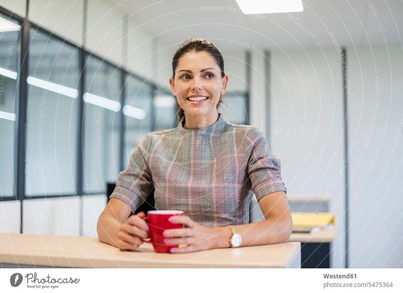 Pretty office worker sitting at desk with red coffee cup Coffee Cup Coffee Cups Seated desks smiling smile employee employess Drink beverages Drinks Beverage