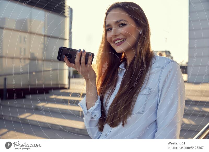 Smiling businesswoman talking on mobile phone while standing on steps color image colour image outdoors location shots outdoor shot outdoor shots sunset sunsets
