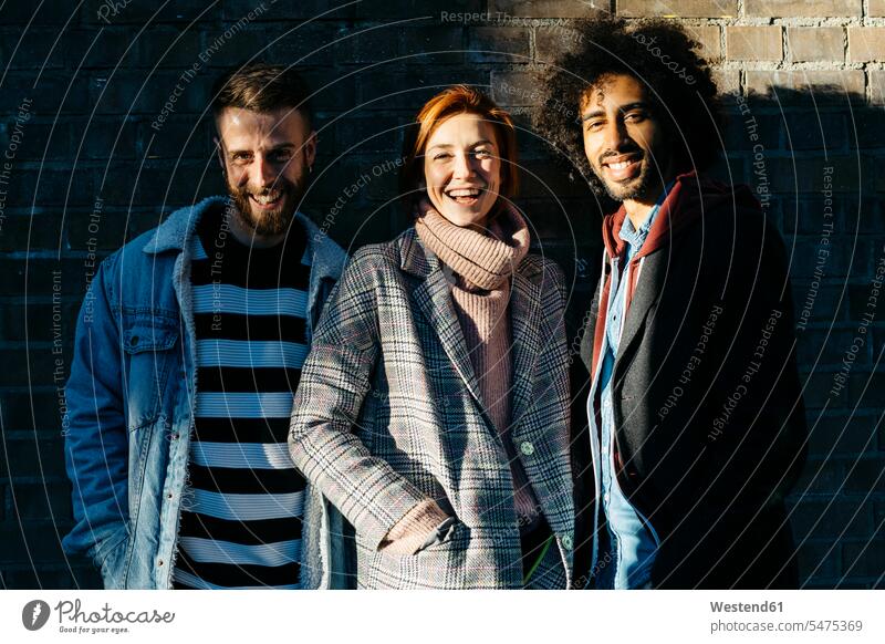 Portrait of three happy friends in shadow at a brick wall happiness brick walls shadows Shades portrait portraits standing friendship fashionable togetherness