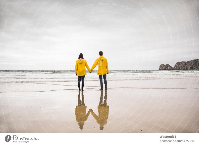 Young woman wearing yellow rain jackets and standing at the beach, Bretagne, France caps hat hats Emotions Feeling Feelings Sentiment Sentiments loving