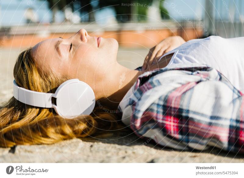 Woman lying on back listening music through headphone during sunny day color image colour image outdoors location shots outdoor shot outdoor shots daylight shot