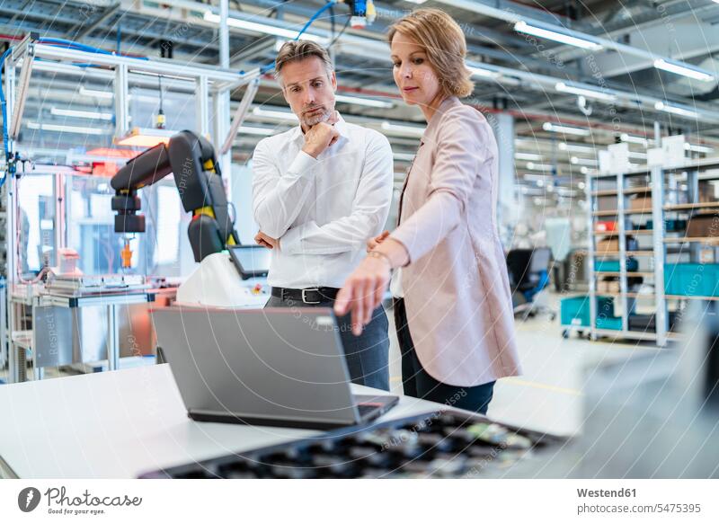 Businessman and businesswoman with laptop talking in a modern factory hall human human being human beings humans person persons caucasian appearance