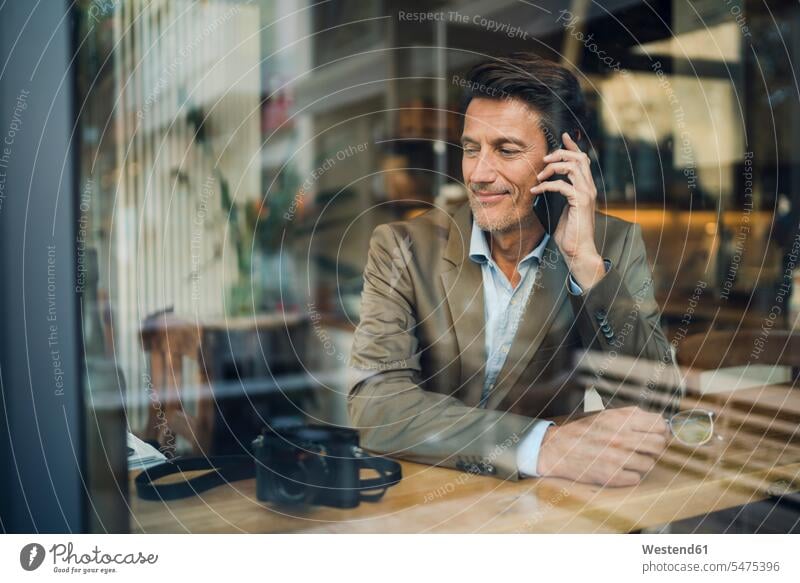Mature businessman sitting in coffee shop, talking on the phone Businessman Business man Businessmen Business men Smartphone iPhone Smartphones Seated smiling