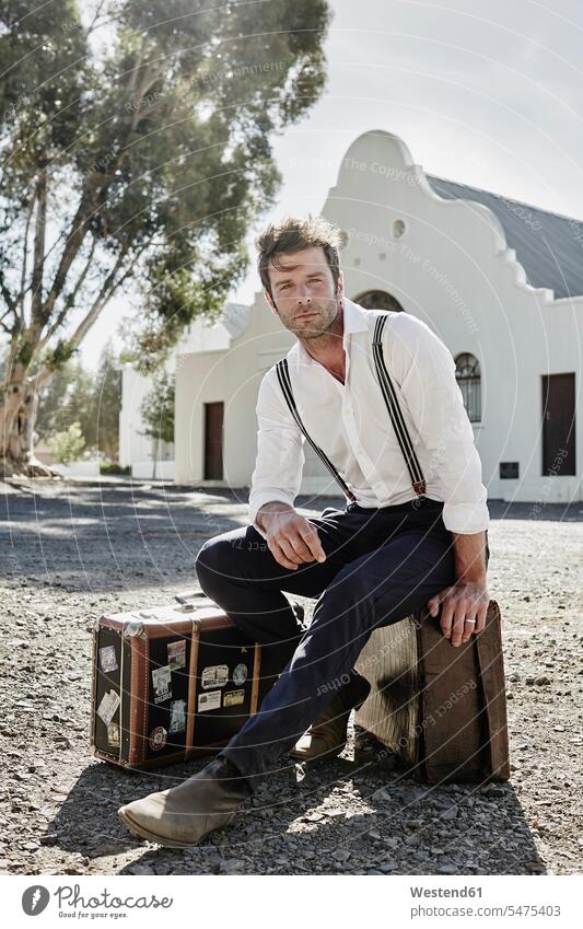 Man in old-fashioned clothes sitting on suitcase in the countryside human human being human beings humans person persons caucasian appearance