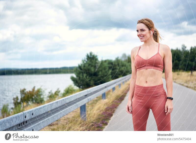 Portrait of smiling sporty woman with wireless earphones at the lakeside hear smile summer time summertime summery relax relaxing relaxation delight enjoyment