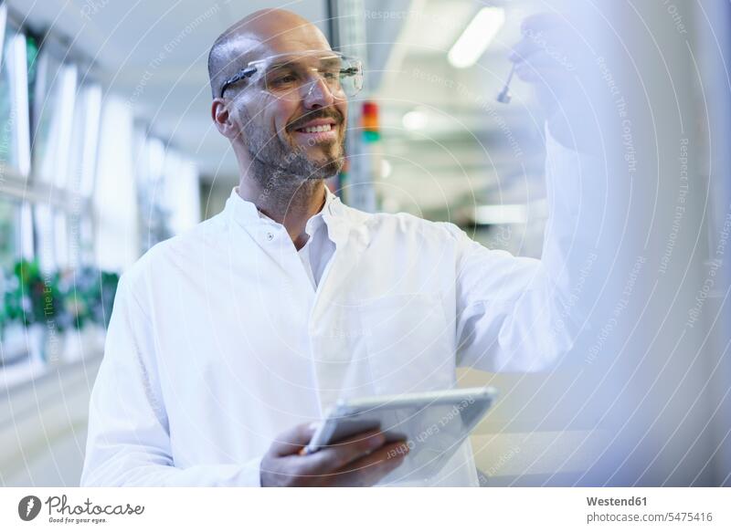 Smiling male scientist looking at sample while holding digital tablet in factory color image colour image indoors indoor shot indoor shots interior