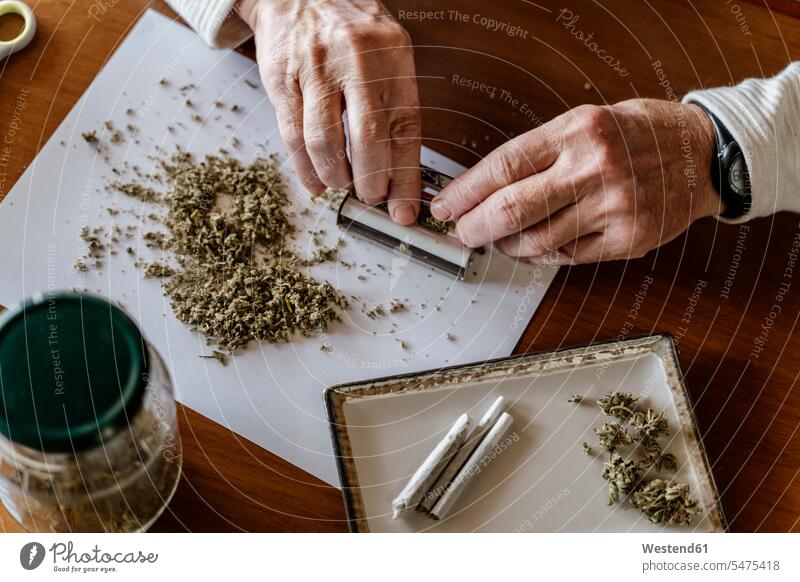 High angle view of senior man rolling weed on table at home color image colour image Spain indoors indoor shot indoor shots interior interior view Interiors day