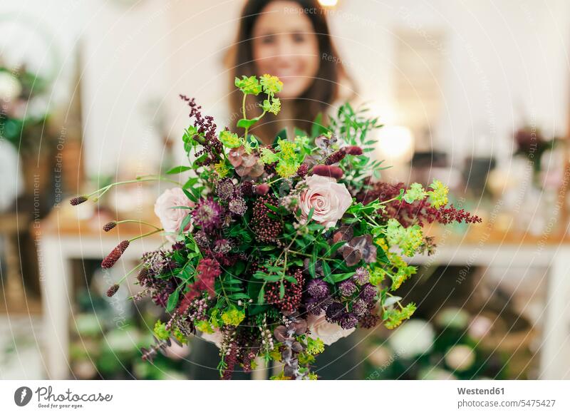 Woman holding bunch of flowers while standing at flower shop color image colour image indoors indoor shot indoor shots interior interior view Interiors smiling