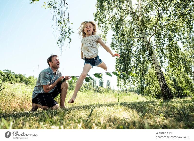 Father with daughter jumping over stick in poppy meadow human human being human beings humans person persons caucasian appearance caucasian ethnicity european