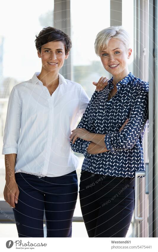 Portrait of two smiling businesswomen at the window in office offices office room office rooms portrait portraits businesswoman business woman business women