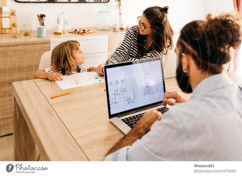 Man using laptop while mother and daughter painting in dining room color image colour image indoors indoor shot indoor shots interior interior view Interiors