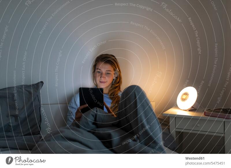 Young woman lying in bed at home at night using tablet human human being human beings humans person persons celibate celibates singles solitary people