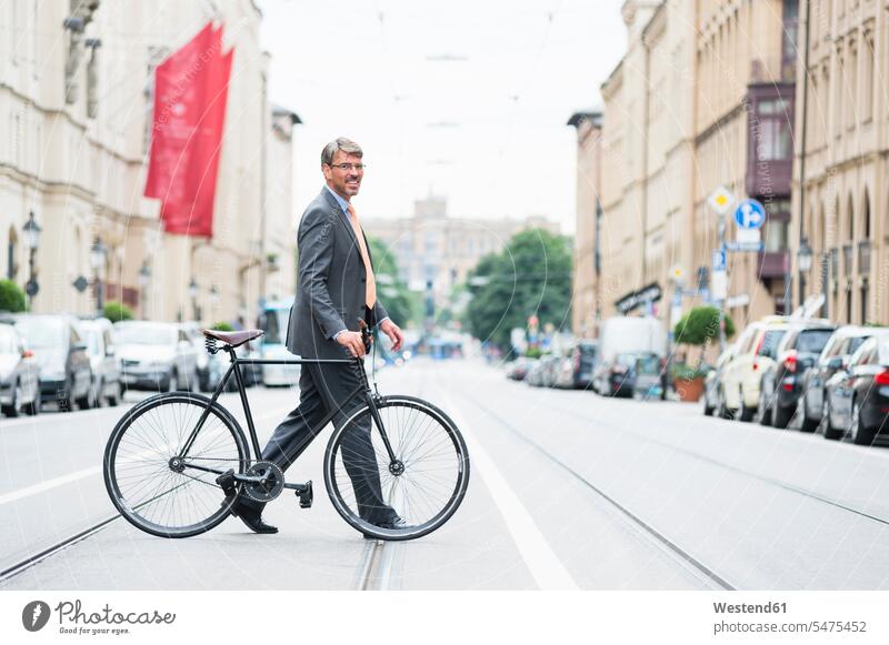 Businessman wearing suit with bicycle crossing road in city color image colour image Germany outdoors location shots outdoor shot outdoor shots day