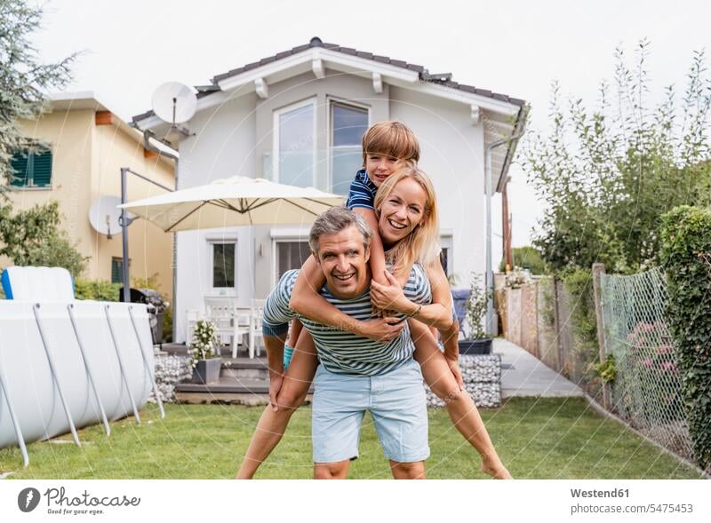 Portrait of father carrying wife and son piggyback in garden smile summer time summertime summery Ardor Ardour enthusiasm enthusiastic excited delight enjoyment