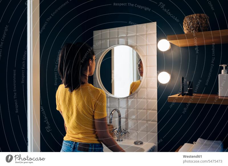 Young woman looking in bathroom mirror human human being human beings humans person persons celibate celibates singles solitary people solitary person bulb