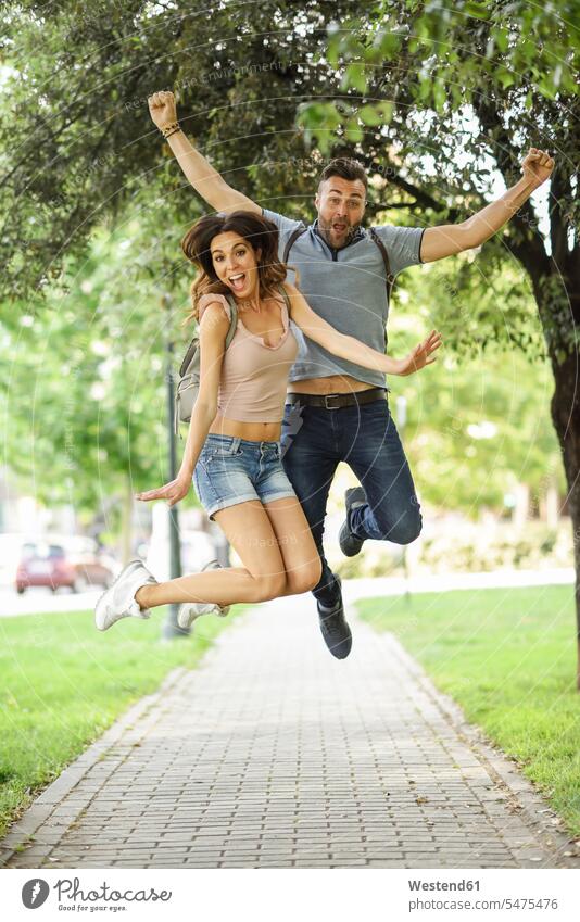 Carefree couple jumping in park happiness happy parks twosomes partnership couples Leaping carefree people persons human being humans human beings jumps motion