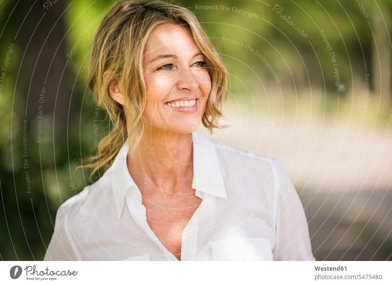 Thoughtful mature businesswoman smiling outdoors during sunny day color image colour image location shots outdoor shot outdoor shots daylight shot