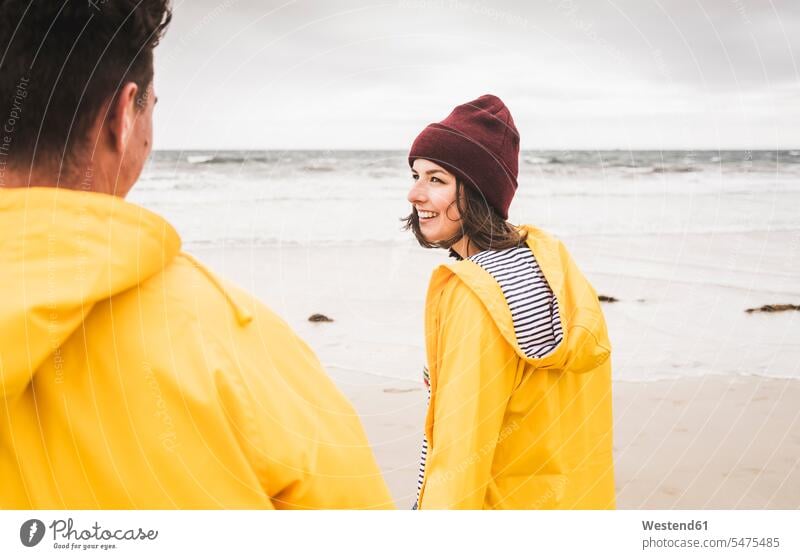 Young woman wearing yellow rain jackets and walking along the beach, Bretagne, France caps hat hats smile delight enjoyment Pleasant pleasure Cheerfulness