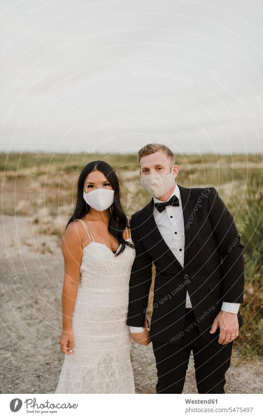 Bride and groom with protective face mask in field during COVID-19 color image colour image outdoors location shots outdoor shot outdoor shots Canada