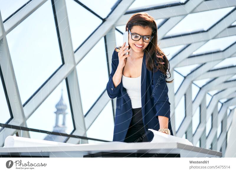 Smiling businesswoman on cell phone looking at plan in office eyeing on the phone call telephoning On The Telephone calling businesswomen business woman