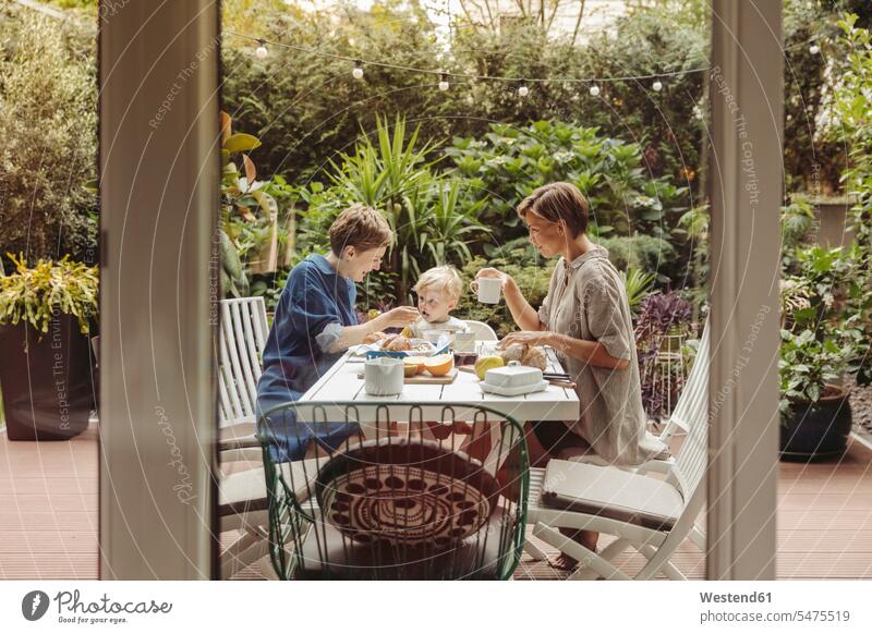 Two happy mothers at breakfast table outdoors with their child mommy ma mummy mama Breakfast Table Breakfast Tables children happiness parents family families