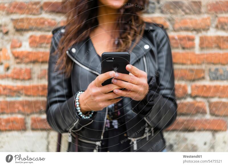 Young woman wearing black leather jacket, using smartphone, brick wall in the background brick walls leather jackets Smartphone iPhone Smartphones use females