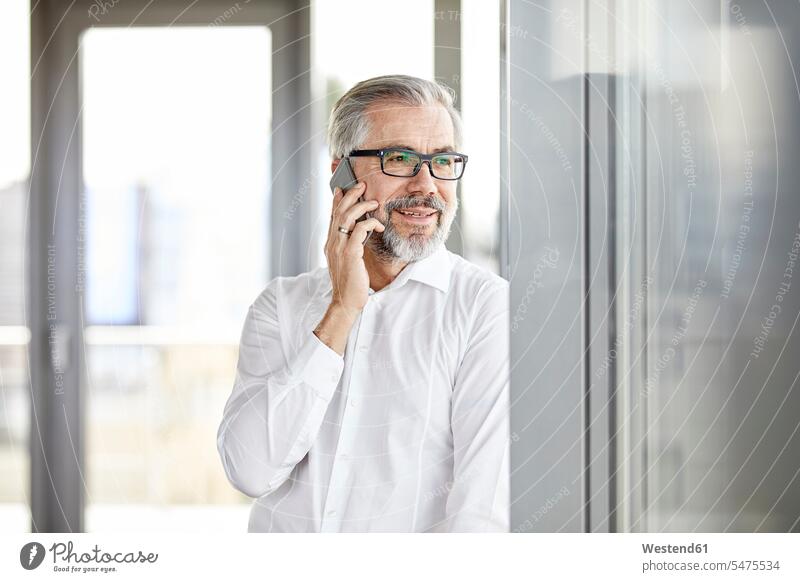 Smiling businessman talking on cell phone at the window standing on the phone call telephoning On The Telephone calling mobile phone mobiles mobile phones