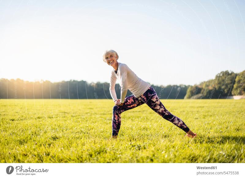 Smiling senior woman stretching on rural meadow meadows females women country countryside smiling smile senior women elder women elder woman old Adults