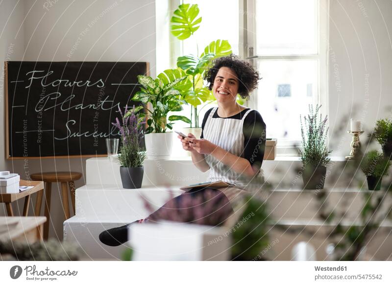 Portrait of smiling young woman using cell phone in a small shop with plants Occupation Work job jobs profession professional occupation human human being
