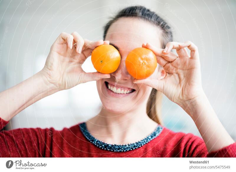 Laughing woman covering her eyes with oranges Orange Citrus sinensis Oranges females women laughing Laughter Citrus Fruit Citrus Fruits Food foods
