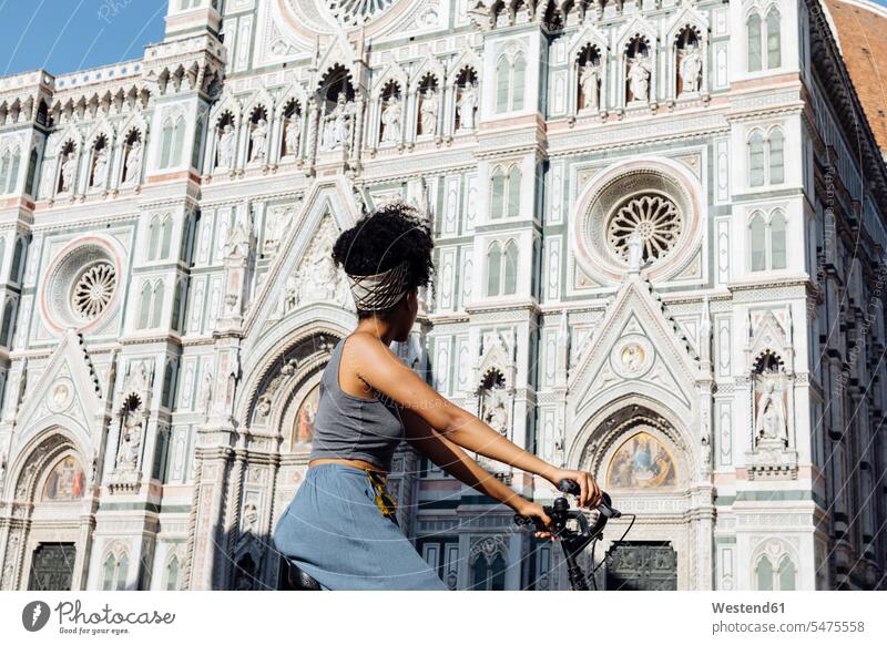 Young woman riding bicycle in front of cathedral, Florence, Italy human human being human beings humans person persons African black black ethnicity coloured