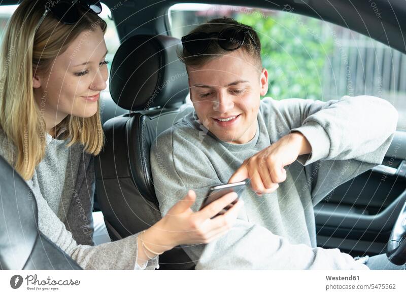 Smiling young couple in a car looking at cell phone human human being human beings humans person persons driver motor vehicles road vehicle road vehicles Auto