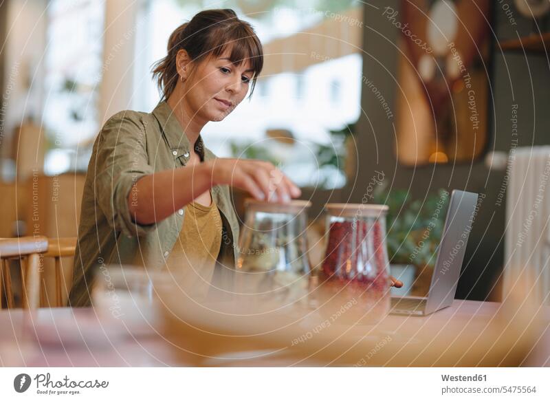 Businesswoman closing glass jars while standing in cafe color image colour image indoors indoor shot indoor shots interior interior view Interiors day