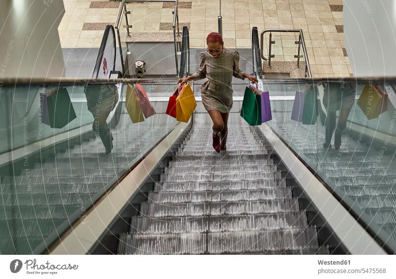 Happy black woman on a funny haircut holding colorful shopping bags walking on the escalators shopping-bag shopping-bags dresses Escalators moving staircase