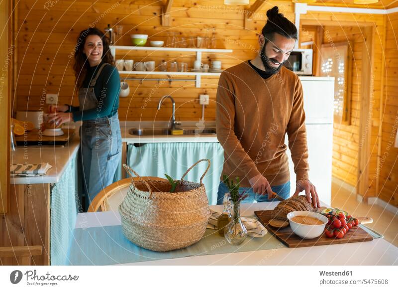 Young man with girlfriend in a wooden cabin cutting bread touristic tourists Bowls smile delight enjoyment Pleasant pleasure indulgence indulging savoring happy