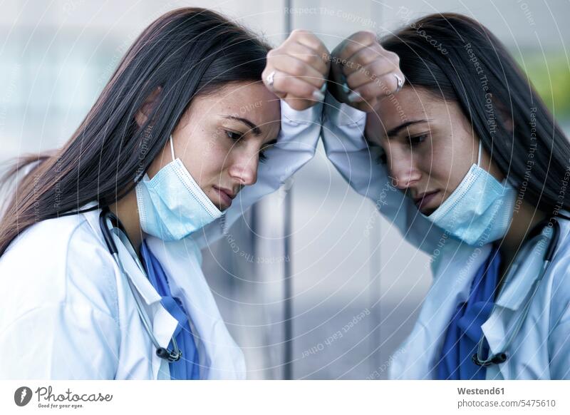 Tired doctor wearing face mask leaning on glass wall of hospital color image colour image outdoors location shots outdoor shot outdoor shots day daylight shot