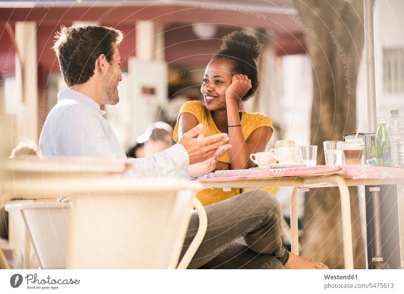 Happy young couple socializing at an outdoor cafe Drinking Glass Drinking Glasses Tables flirt Flirtation smile Seated sit speak speaking talk seasons