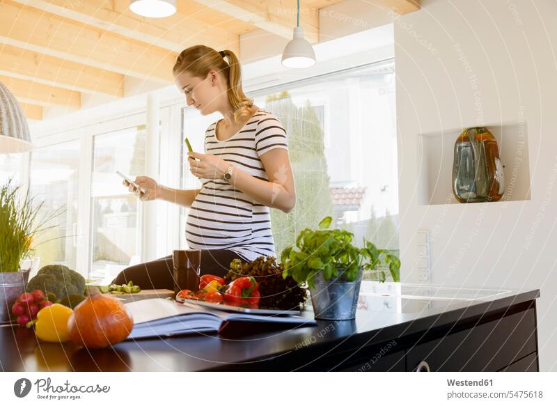 Pregnant woman in kitchen at home using cell phone mobile phone mobiles mobile phones Cellphone cell phones females women pregnant Pregnant Woman telephones