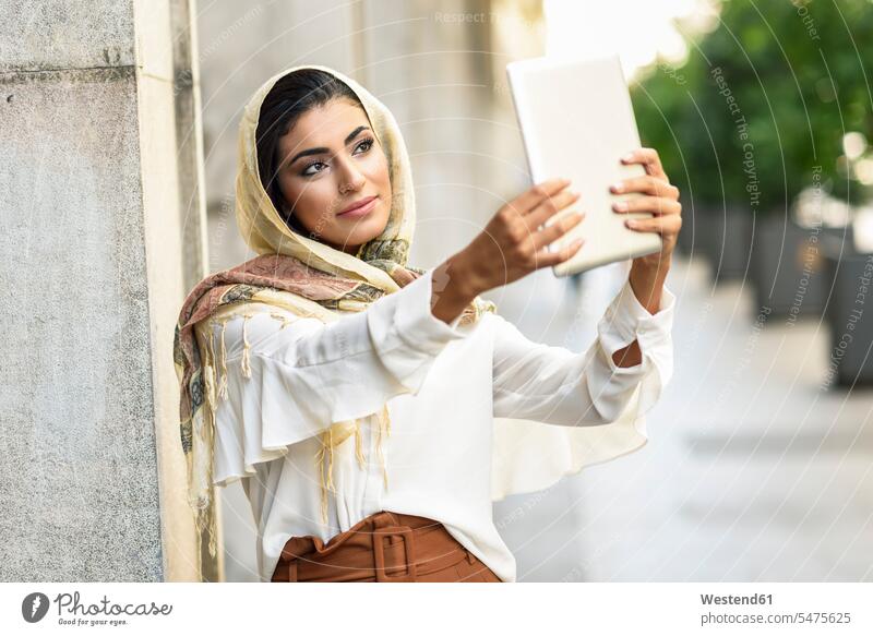 Spain, Granada, young muslim woman wearing hijab using digital tablet computer outdoors headscarf head scarf head scarves Head Scarf head cloths headscarves
