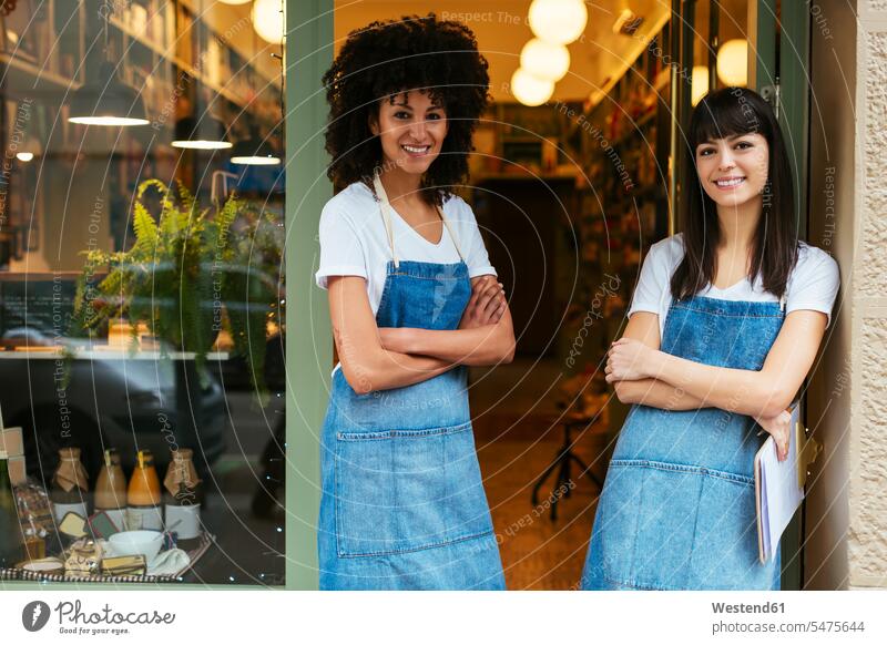 Portrait of two smiling women standing in entrance door of a store portrait portraits smile shop entry door entrance doors woman females retail trade trading