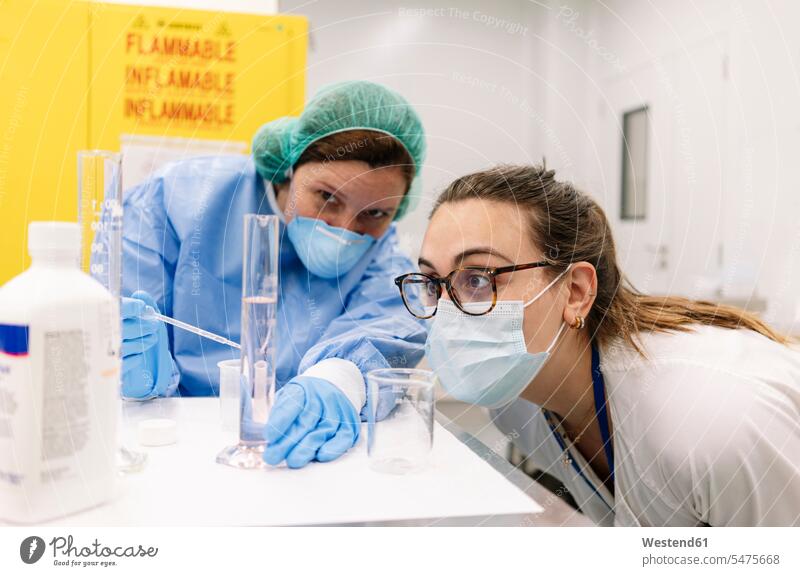 Female pharmacists examining chemical in graduated cylinder at laboratory color image colour image Spain indoors indoor shot indoor shots interior interior view
