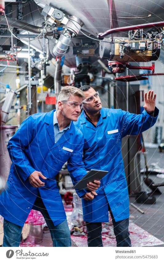 Male coworkers with digital tablet discussing while examining machinery in factory color image colour image indoors indoor shot indoor shots interior