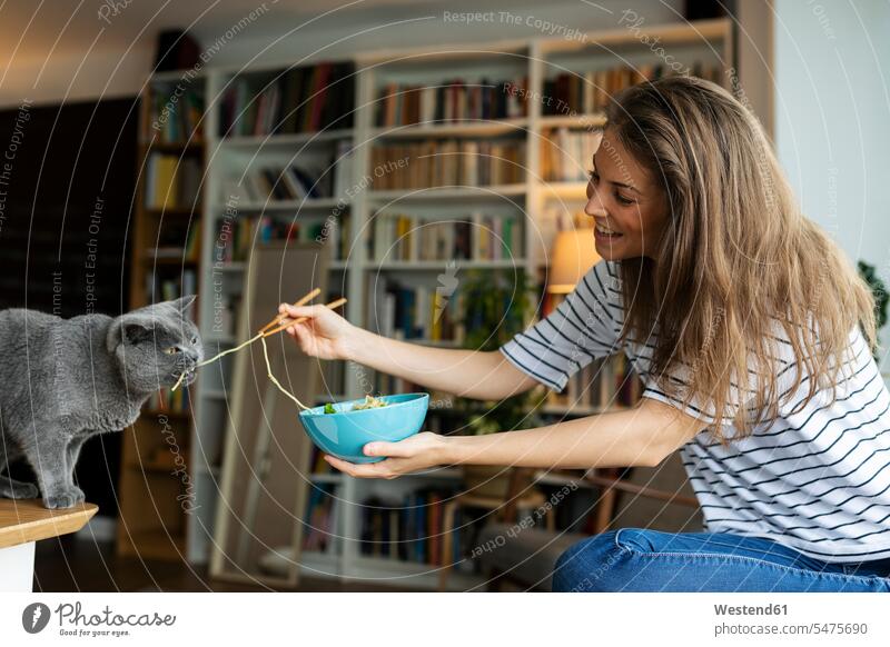 Smiling young woman feeding spaghetti to cat while sitting at home color image colour image Spain casual clothing casual wear leisure wear casual clothes