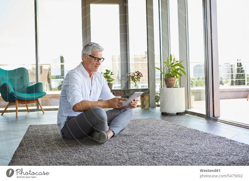 Mature man sitting on carpet at home using tablet digitizer Tablet Computer Tablet PC Tablet Computers iPad Digital Tablet digital tablets men males relaxed