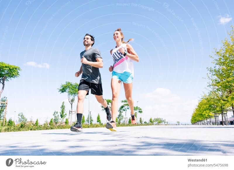 Mid adult couple running on road against blue sky during sunny day color image colour image Spain outdoors location shots outdoor shot outdoor shots