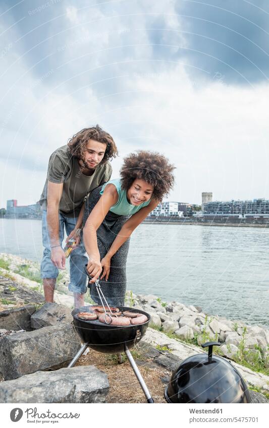 Germany, Cologne, couple having a barbecue at the riverside Barbecue BBQ Barbeque riverbank twosomes partnership couples water's edge waterside shore people