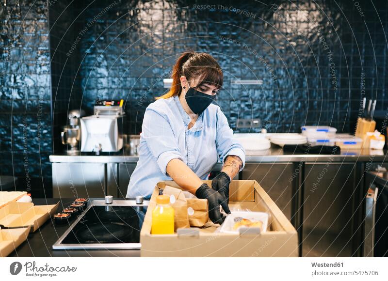 Female chef wearing face mask while keeping take out food in cardboard box at restaurant kitchen counter color image colour image indoors indoor shot