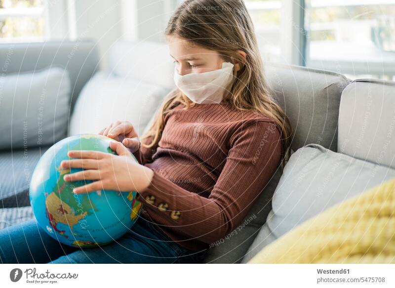 Girl reading globe while wearing face mask on sofa at home color image colour image indoors indoor shot indoor shots interior interior view Interiors day