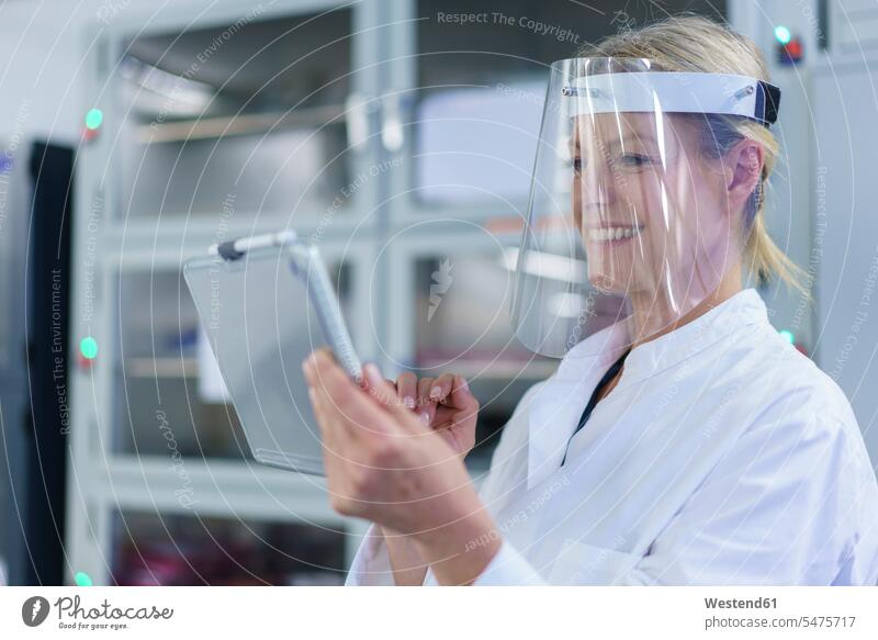 Smiling mature female scientist wearing protective face shield while using digital tablet at laboratory color image colour image indoors indoor shot